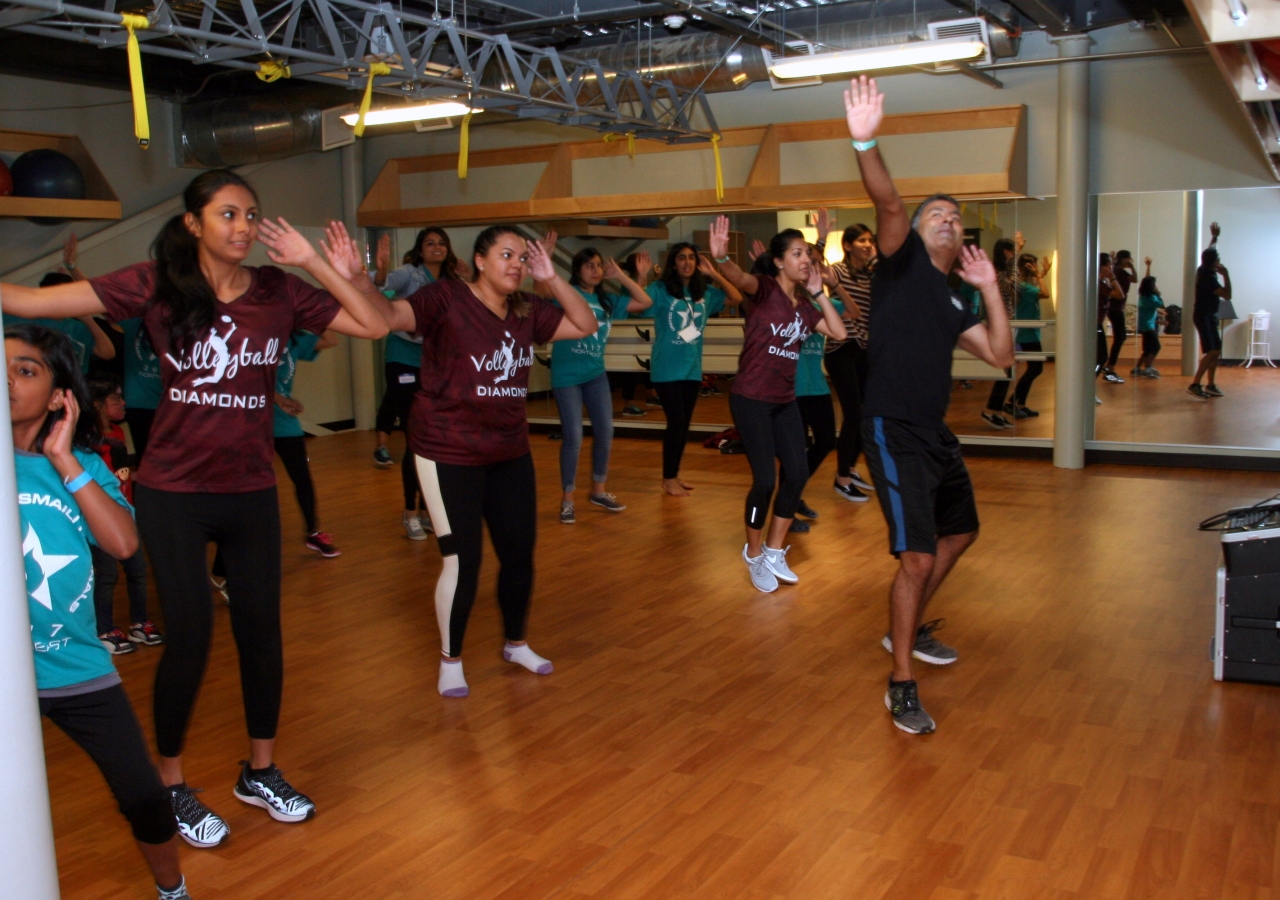 A room full of volunteers, athletes, and spectators thoroughly enjoying a Masala Bhangra class led by Rizwan Dhanidina. 