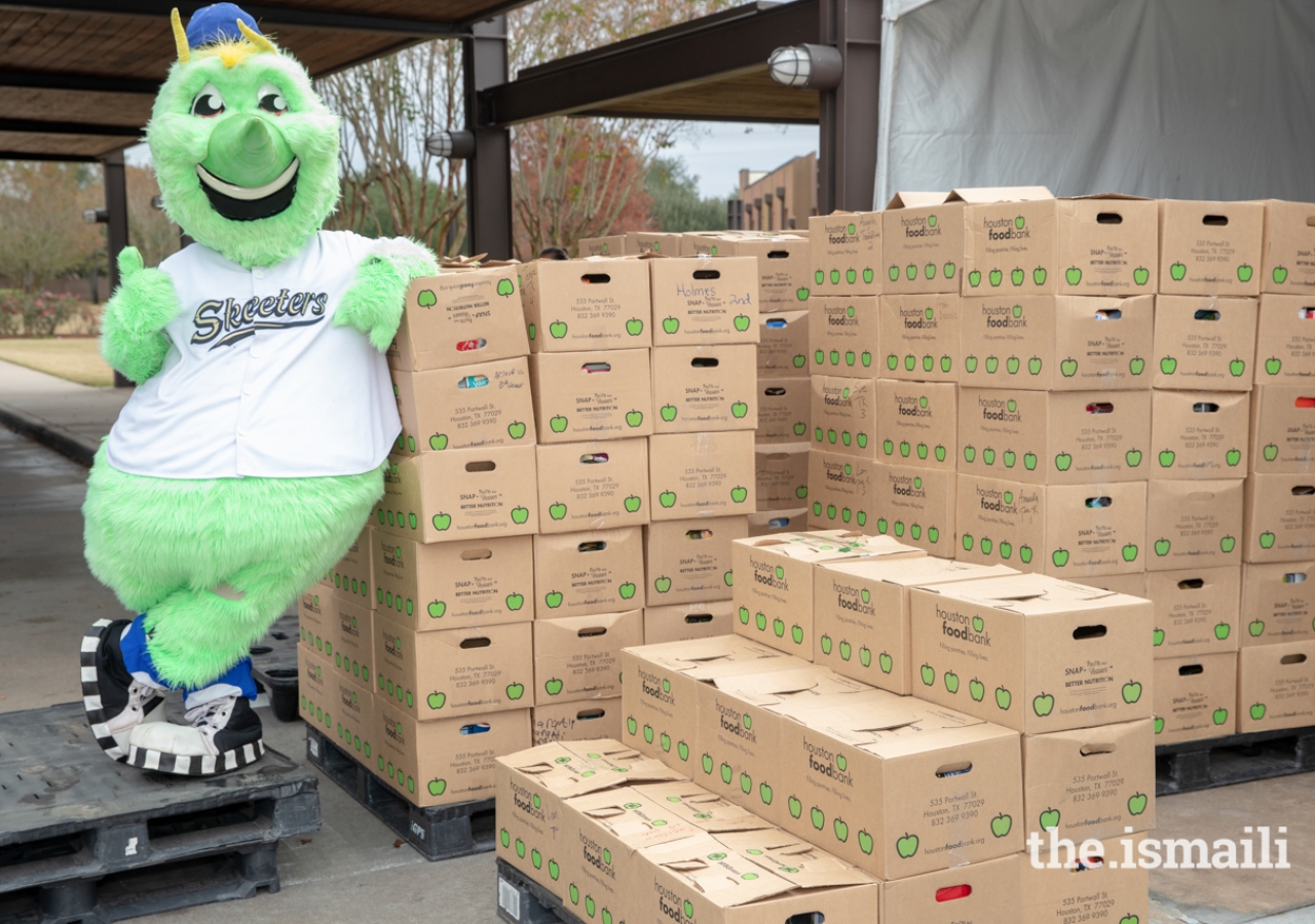 Swatson, mascot of the Sugar Land Skeeters, posing next to a few of the donated food items., Over 30,000 pounds of food were collected at the Ismaili Jamatkhana and Center and donated to the East Fort Bend Human Needs Ministry in Stafford, Texas. 