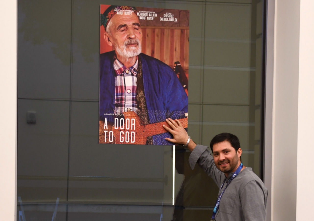 Maruf Noyoft next to a poster of his film, "A Door to God."