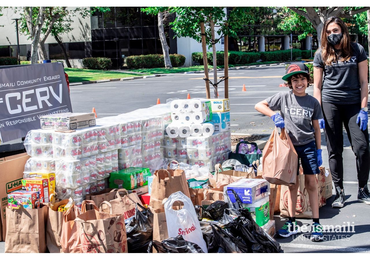 A young I-CERV volunteer holds bags of donated items in front of the donation drop-off area at Los Angeles HQ Jamatkhana.