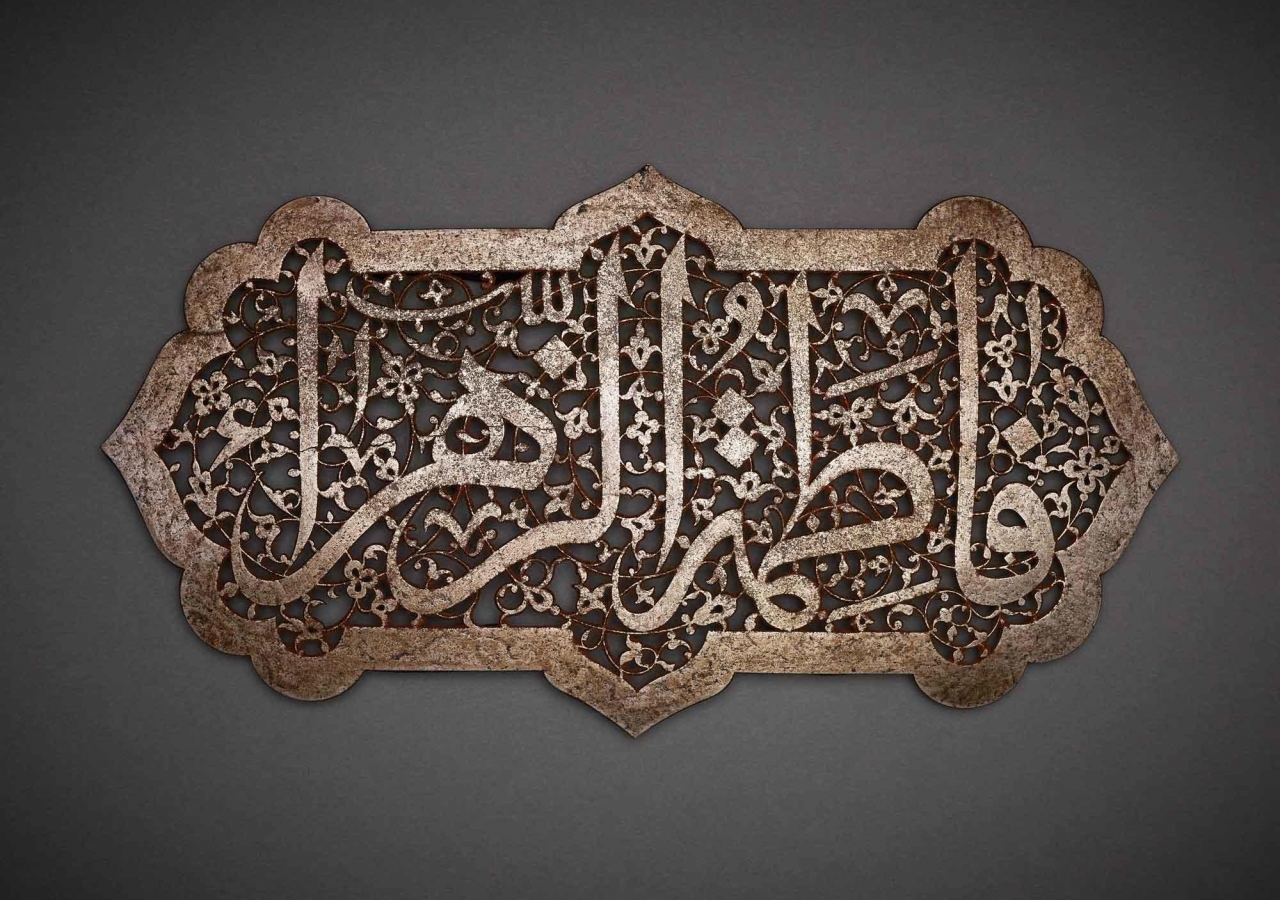 The inscription Fatima al-Zahra’ (“Fatima the Radiant”), the name of the Prophet’s daughter and her epithet, is carved out in an elegant contrast between the solid lines of the magisterial thuluth script and the intricately carved floral spiral that forms its background.