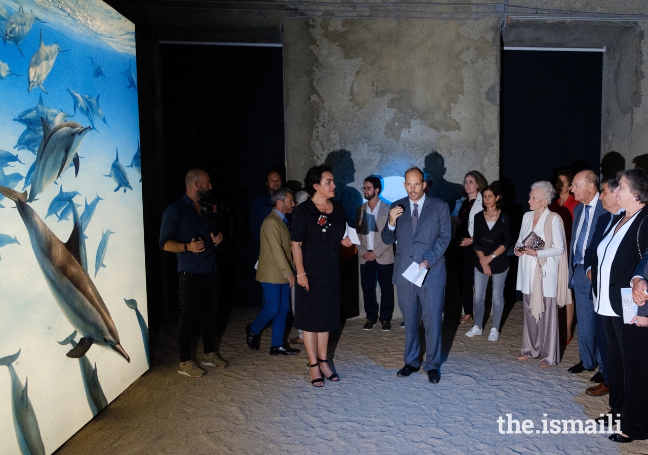 Prince Hussain presents a photo of dolphins to Marta Lorenço, Director of Portugal’s National Museum of Natural History and Science, as Prince Amyn and guests look on.