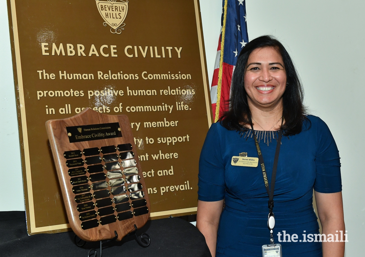 Sharmin Barolia stands in front of a plaque with the names of past honorees of the Embrace Civility Award.