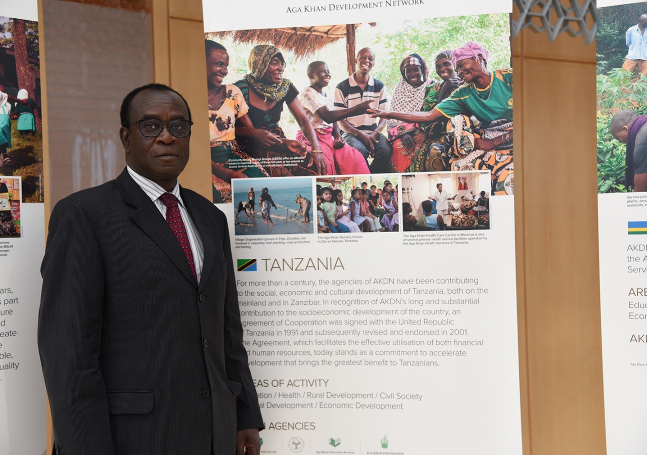 Tanzanian Ambassador Jack Mugendi Zoka stands next to a banner describing the work of the AKDN in his country. AKDN / Safiq Devji