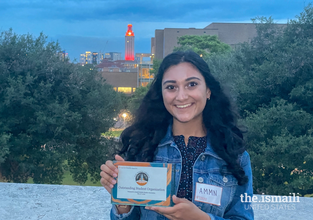 Ammn Meghani, President of the Ismaili Muslim Students Association, with the award for Outstanding Student Organization amidst the backdrop of the UT Austin tower.