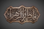 The inscription Fatima al-Zahra’ (“Fatima the Radiant”), the name of the Prophet’s daughter and her epithet, is carved out in an elegant contrast between the solid lines of the magisterial thuluth script and the intricately carved floral spiral that forms its background.