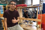 Saif Punjwani standing next to the prototype of his FIRST Robotics Competition team's lift mechanism. Saif led the creation of the lift mechanism, which was a crucial component that allowed his team's 2019 robot to lift above the ground and reach a new level. 