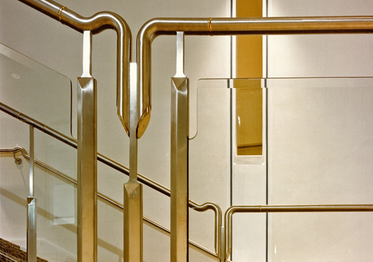 Detail of the handrail in stainless steel, brass and plate glass, which runs along the main stair.