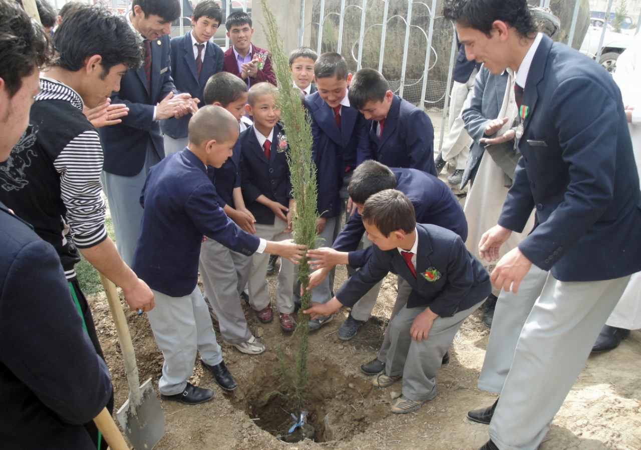 Older volunteers help their junior counterparts to plant a tree, and teach them about the importance of caring for the environment.