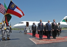 Mawlana Hazar Imam with President Mahmoud Eboo of the Ismaili Council for USA and Chris Young, Chief of Protocol for the State of Georgia, listening to the Honor Cordon Band from the Youth Challenge Academy as they perform the US National Anthem and the N