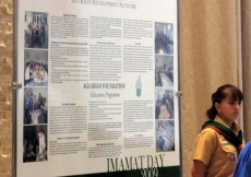 An Aga Khan Scout stands next to one of the educational display boards at the Imamat Day Reception.