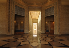 A view from the Main Entrance shows a seating alcove on the left, a reception desk on the right, and the axial corridor of the Administration area leading to the Great Courtyard.