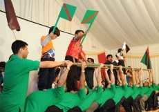 Volunteers form a human bridge, atop which young children wave the Ismaili and Qatari flags.