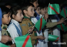 Young scouts and guides waving the national flag, the Ismaili flag and the Diamond Jubilee flag.