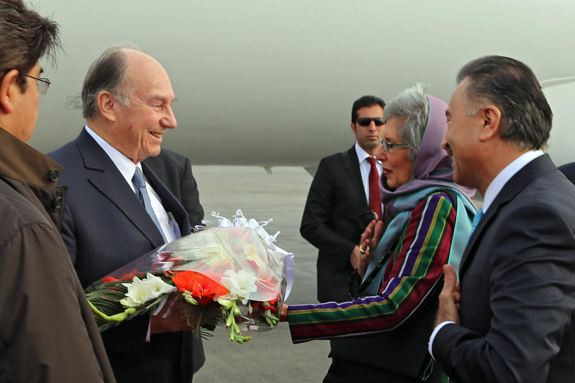 Mawlana Hazar Imam is presented with a bouquet of flowers by AKDN Resident Representative Nurjehan Mawani upon his arrival in Kabul, as Ismaili Council for Afghanistan President Shair Baz Hakemy looks on. Photo: AKDN / Muslim Khuram